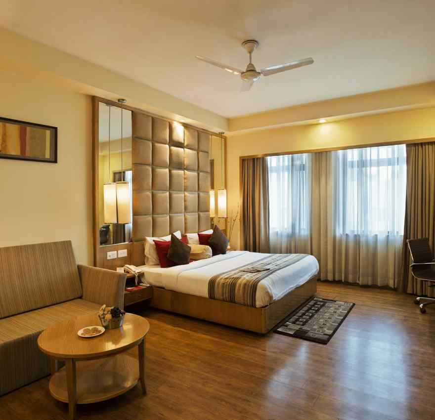 A suite at The Manor Bareilly with a plush sofa and a large window that allows natural light to fill the space
