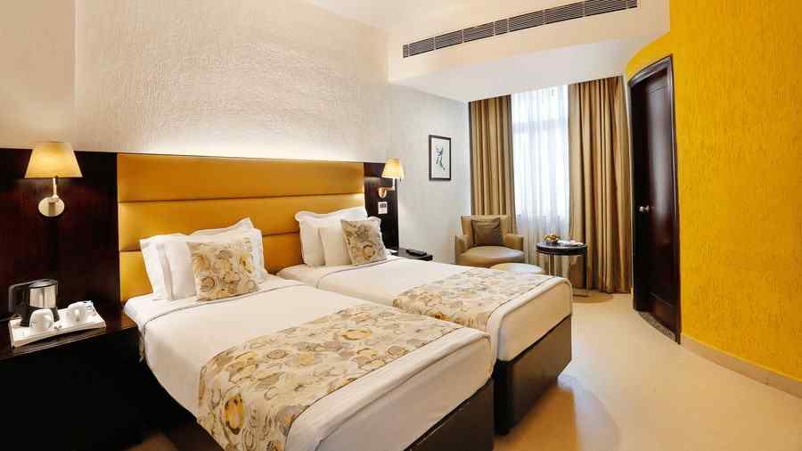 A spacious twin bedroom at The Manor, Bareilly, featuring two neatly arranged single beds and a window that fills the room with natural light
