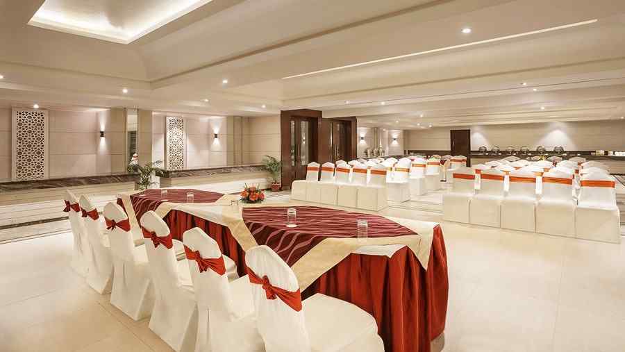 A neatly arranged event space with white covered chairs and burgundy accents prepared for a social event - The Manor, Bareilly