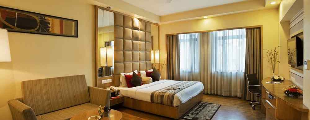 A suite at The Manor Bareilly with a plush sofa and a large window that allows natural light to fill the space