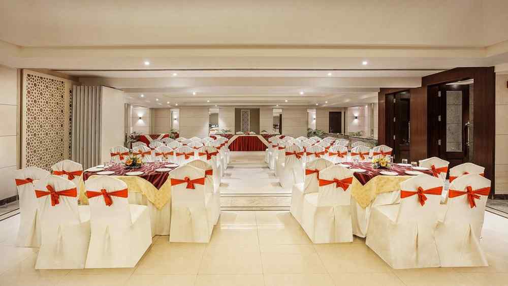 an image of an event space showing a well-spaced seating arrangement with white chairs tied with red bows - The Manor, Bareilly