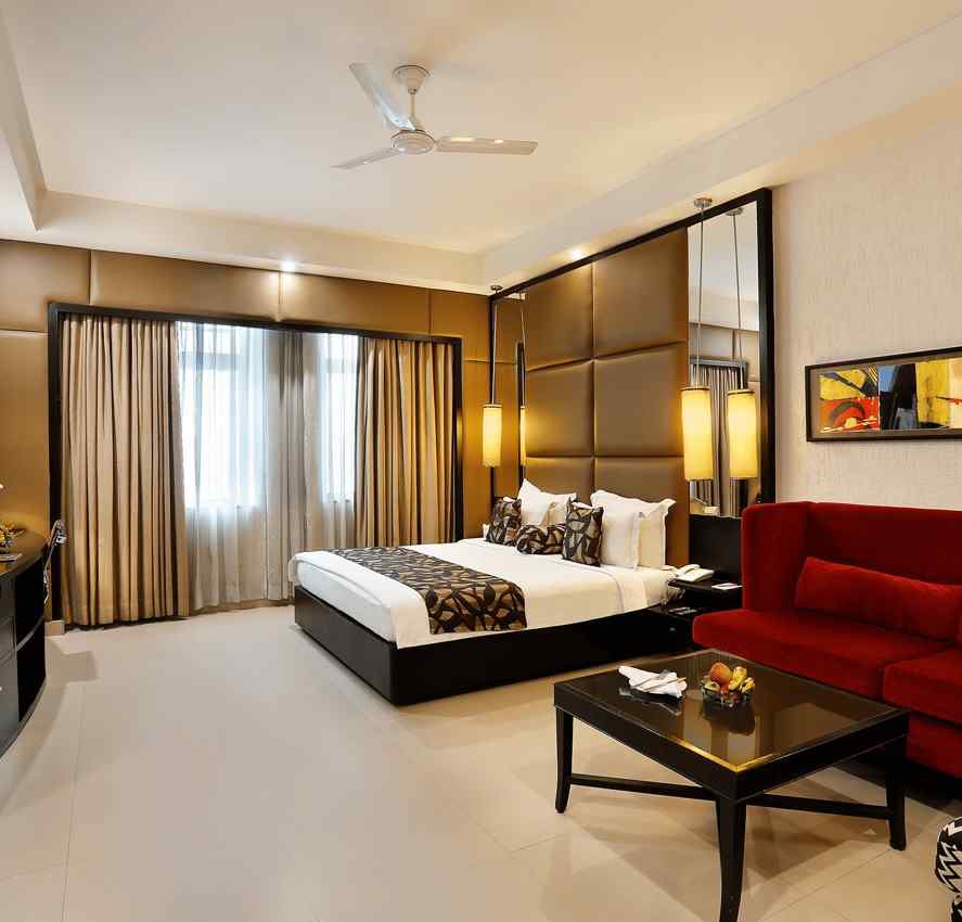 A spacious junior suite with a sleek design, featuring a large bed, red sofa at The Manor, Bareilly
