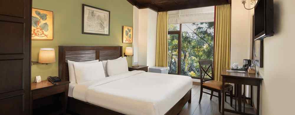 An image of a bedroom with double size bed, bedside table on either side, photos hanged on the wall and four windows from which natural lights are coming in - The Riverview Retreat,  Corbett