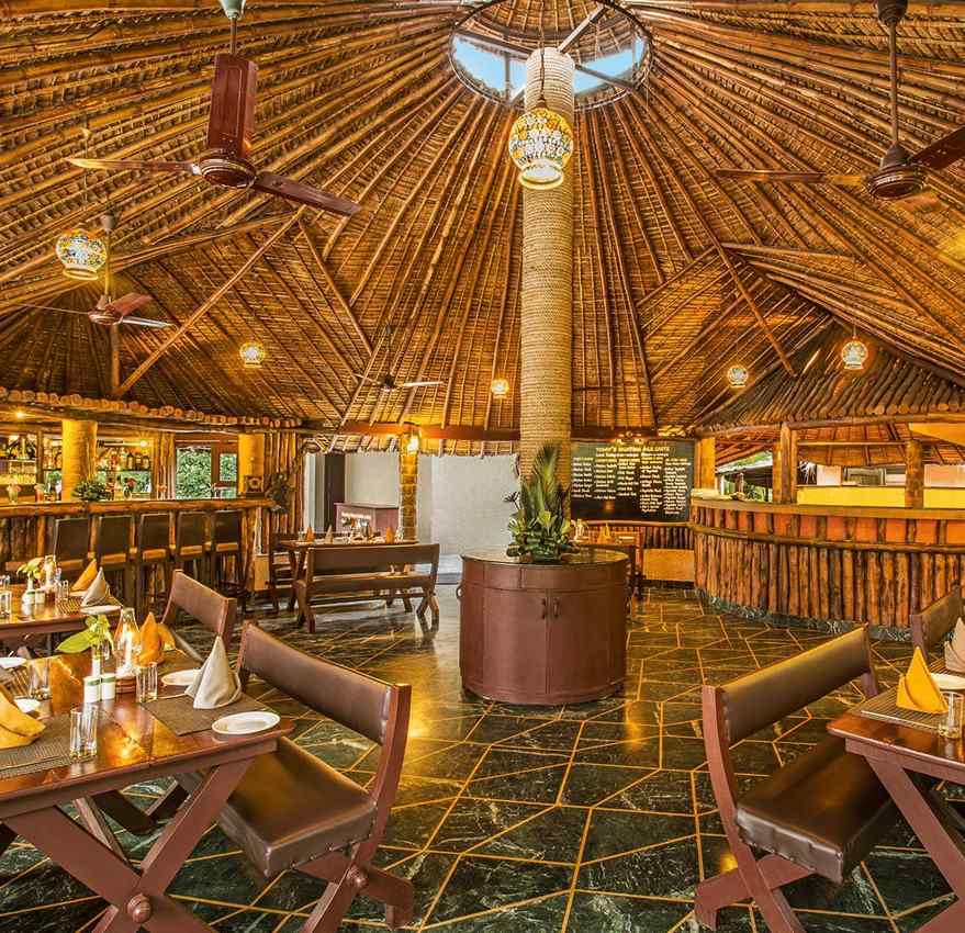 An image of a bar with wooden interiors, wooden chairs and tables, with plants filled at every corner - The Riverview Retreat, Corbett