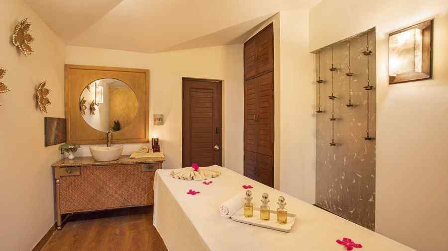 An image of a room with a massage bed, a cabinet with mirror on the wall, and various other spa products kept on a bed