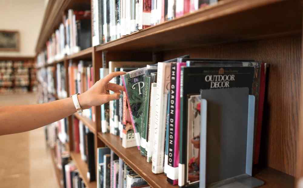 A person selecting a book from a shelf at a Library