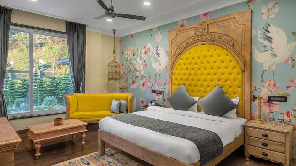 A cozy deluxe bedroom with a comfortable bed and colourful wall decor with a large window, captured in day light - atman, daramshala