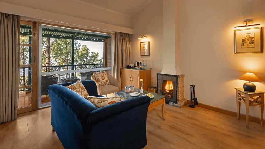 Premium Cottage sitting area with a comfy sofa, beautiful view through window and fireplace in front of sofa at Baikuth resort, kasauli.