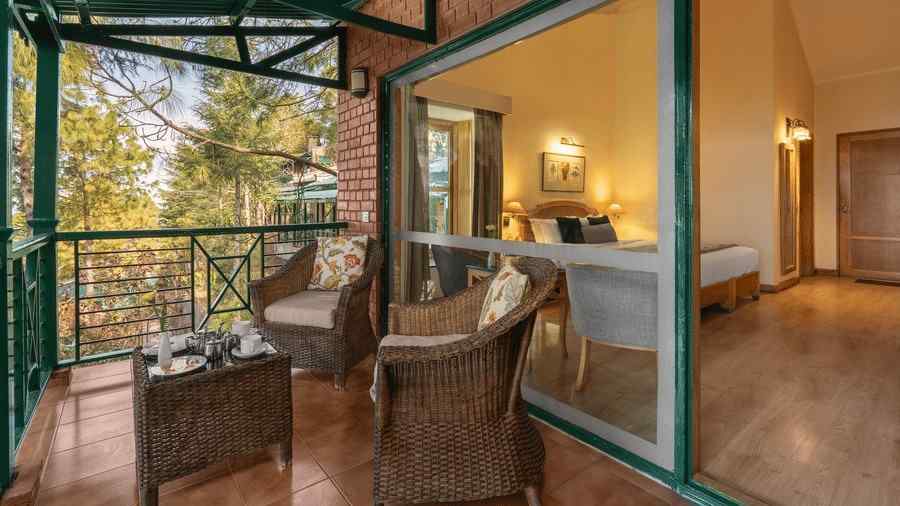 A balcony featuring two wooden chairs and a small table, offering a view of the room interior and the surrounding scenery