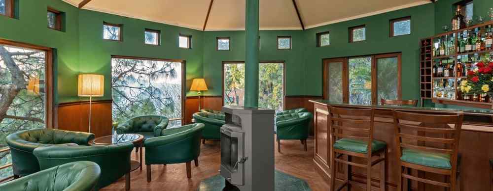 A bar featuring a wooden and green decor, with high chairs and sofas arranged comfortably with warm light lamps -  Baikunth resort, kasauli 