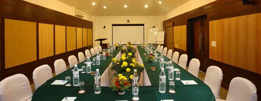  A spacious meeting hall featuring a large table set with water bottles and floral centre pieces, surrounded by neatly arranged chairs -  Baikunth resort, kasauli 