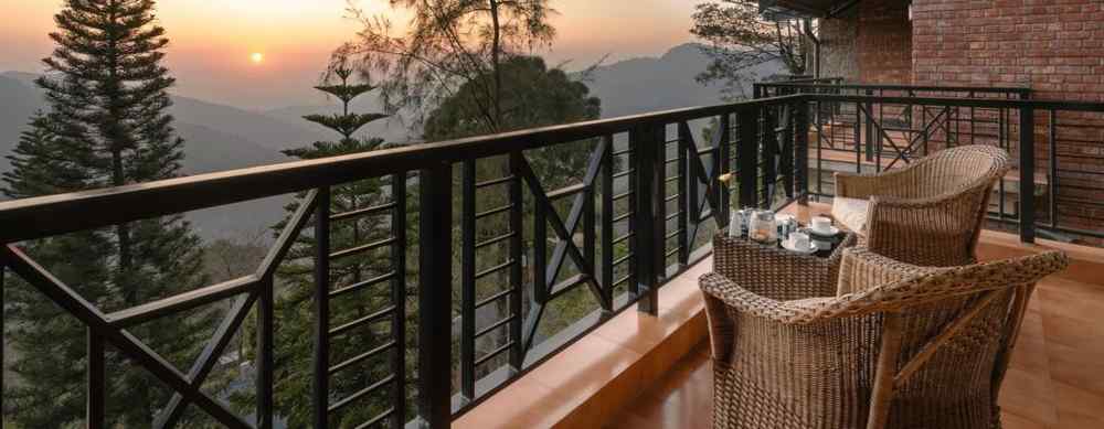 Two wooden chairs and a table set on an open balcony with a sunrise view -  Baikunth resort, kasauli 