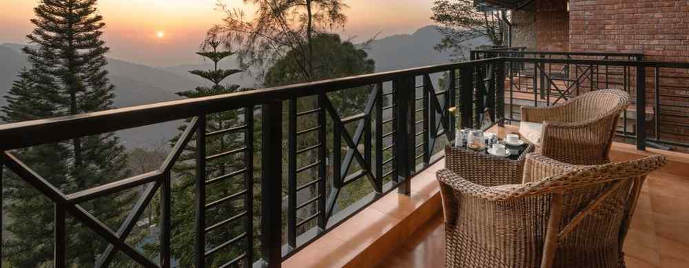 Two wooden chairs and a table set on an open balcony with a sunrise view - Baikunth resort, kasauli 