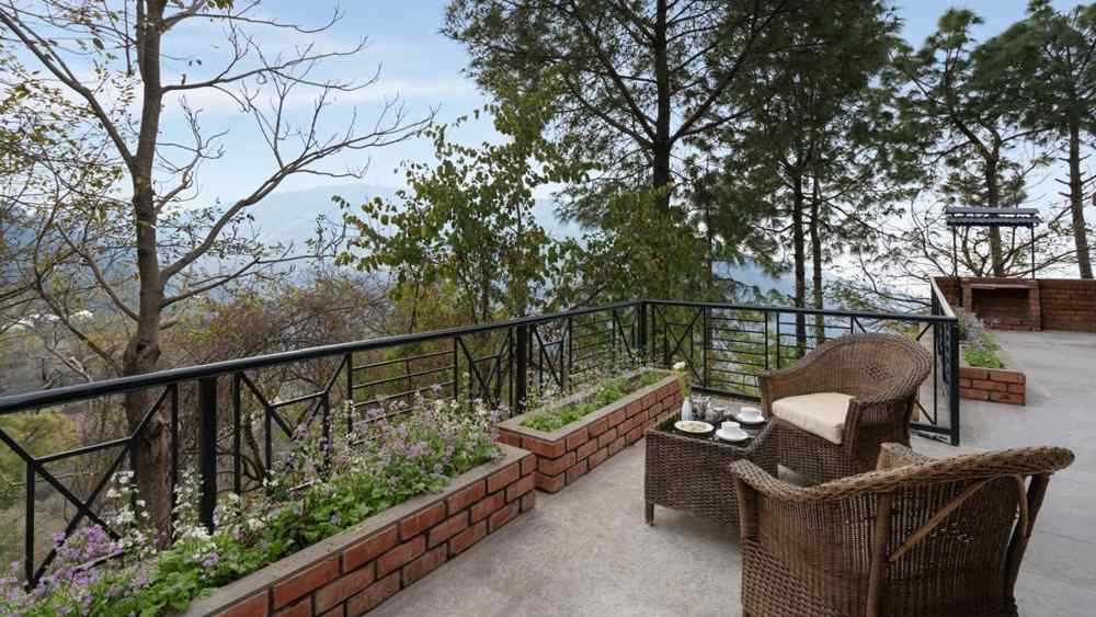 Two wooden chairs and a table set on an open balcony, inviting relaxation -  Baikunth resort, kasauli 