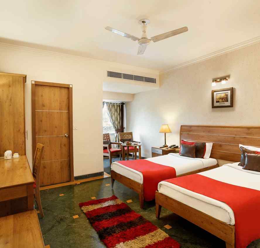 A twin bedroom featuring a floor mat, side tables, a mirror on the wall, and a small sitting area with two chairs