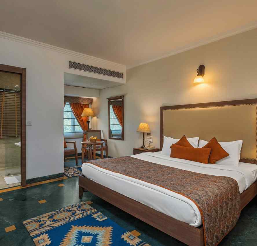 A bedroom with a large bed with side drawers placed on both sides of the bed, with an overhead lamp and side lamps - The Manor, Kashipur