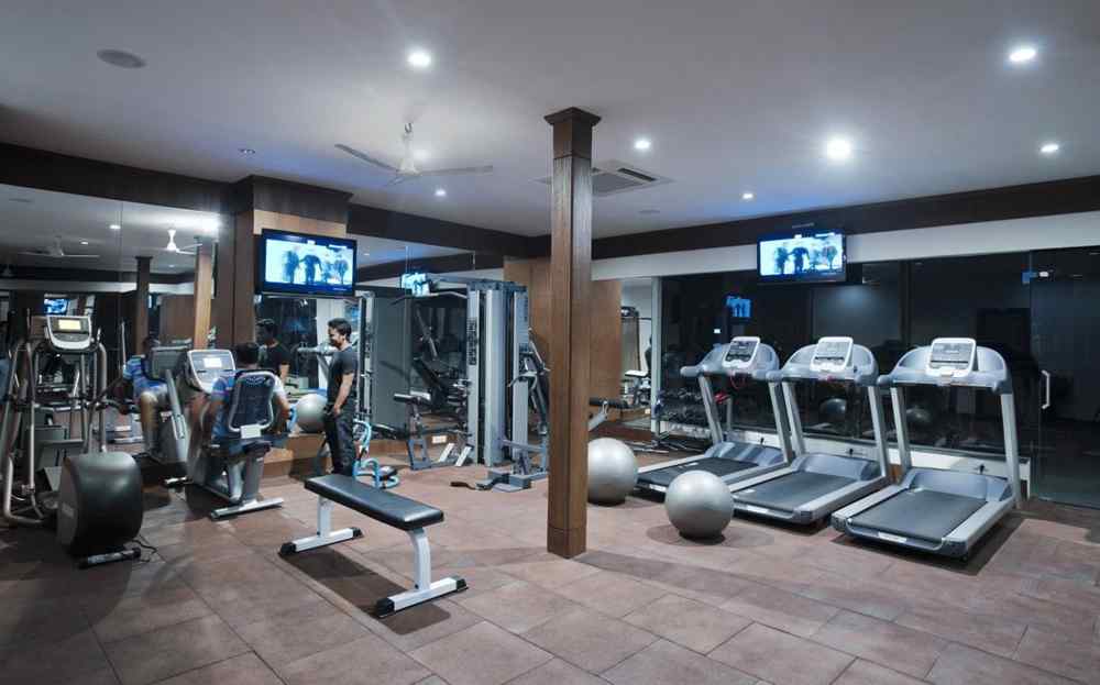 An image of a gym filled with various machines and equipment, showcasing a person standing while observing another individual engaged in a workout.