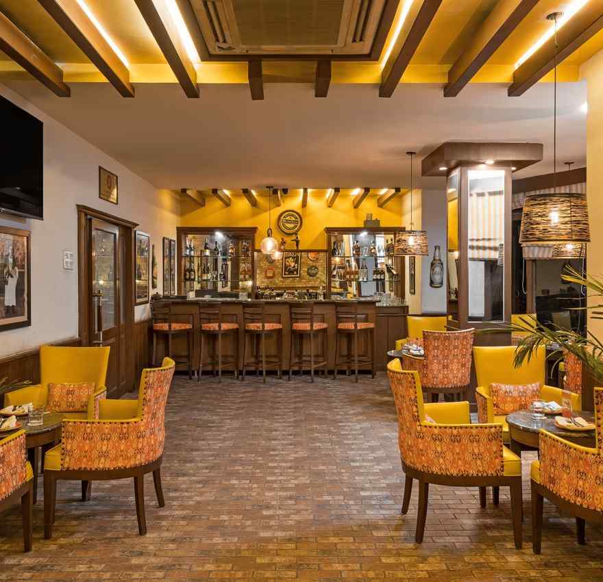 a view of clusters of chairs and tables with a bar counter at the end of the room - The Manor, Kashipur