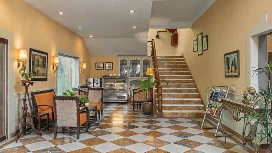 a lobby of a hotel with stairs leading up to the rooms on the right and chairs and tables for sitting on the left - The Manor, Kashipur