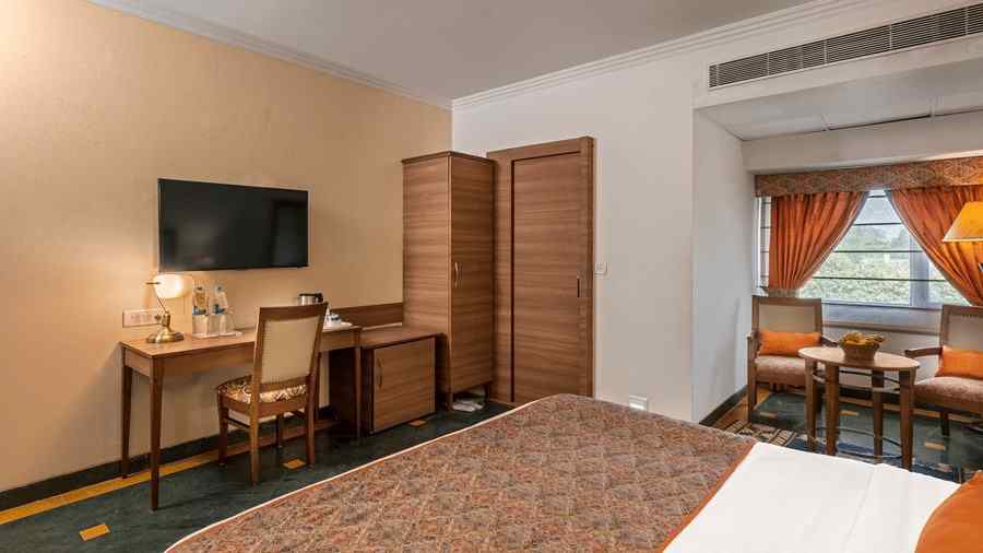 side view of a bedroom with a bed facing a television, below which is a workdesk and chair and a wardrobe beside it - The Manor, Kashipur