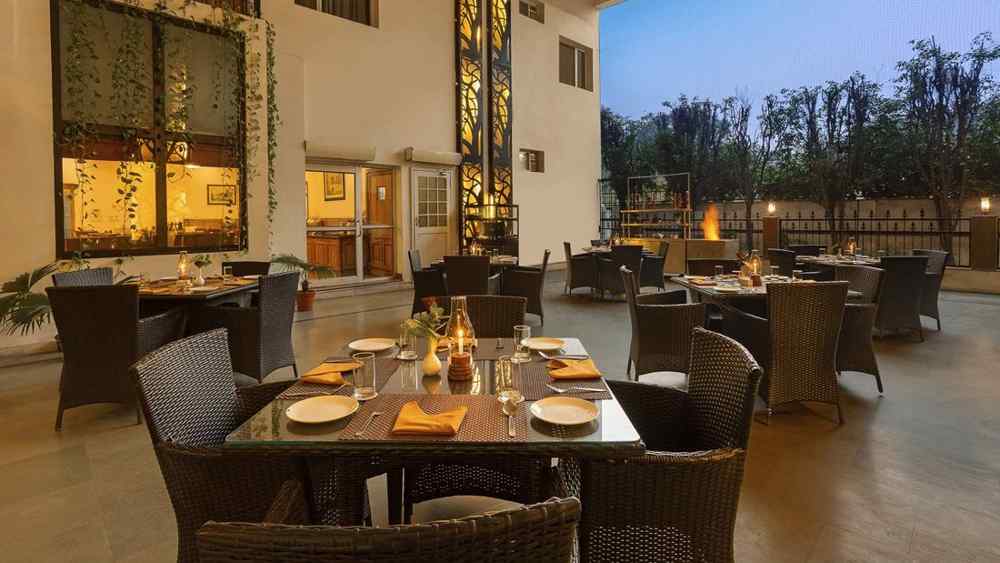 An open dining space on a terrace, featuring tables and chairs arranged with plates and cutlery, illuminated by soft lighting in the evening ambiance