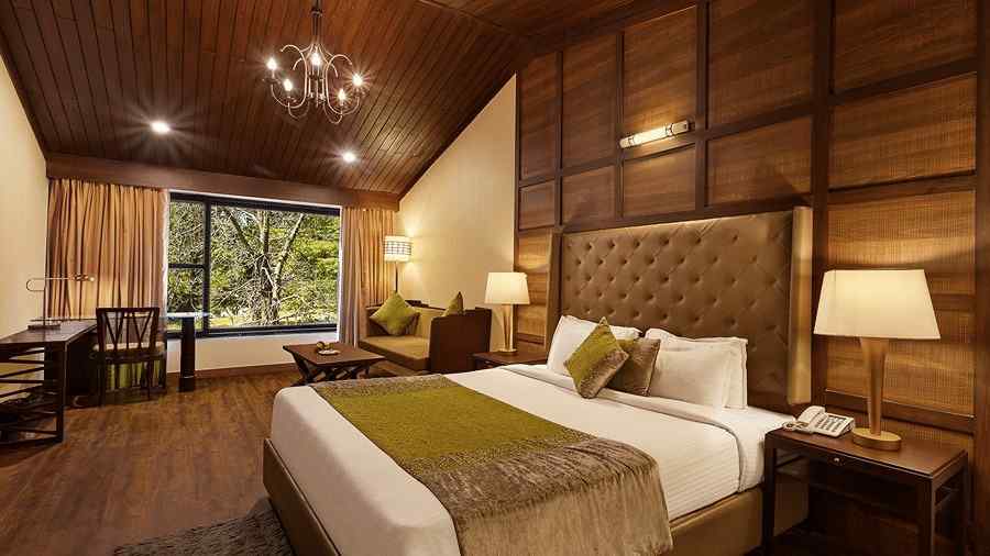 A bedroom with a large bed and a workdesk and chairs on the corner of the room, with large windows with trees visible - The Earl's Court, Nainital
