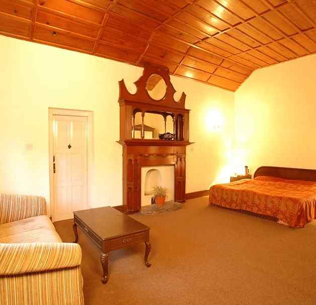 An image of a well lit Heritage Room with a bed , an almirah with mirror attached and has a few drawers, and on one corner there is a sofa with one centre table - The Earl s Court Nainital vrhc3h