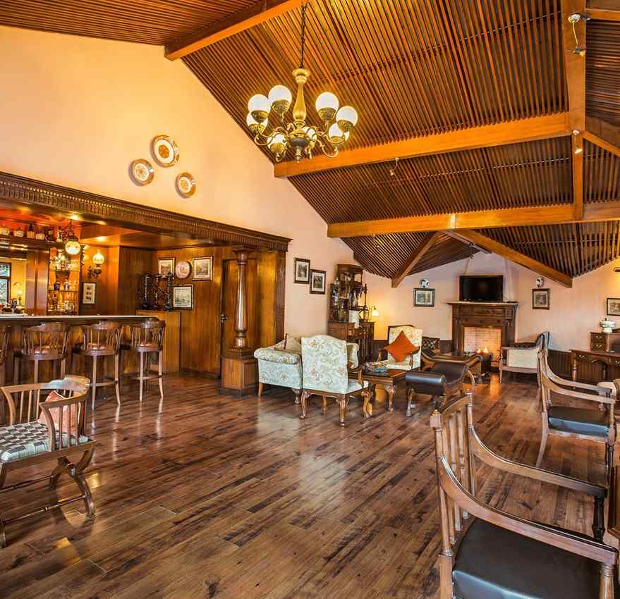 An image of indoor view of the bar at The Naini Retreat, Nainital, with sets of chairs and tables placed around the chandelier on the ceiling.
