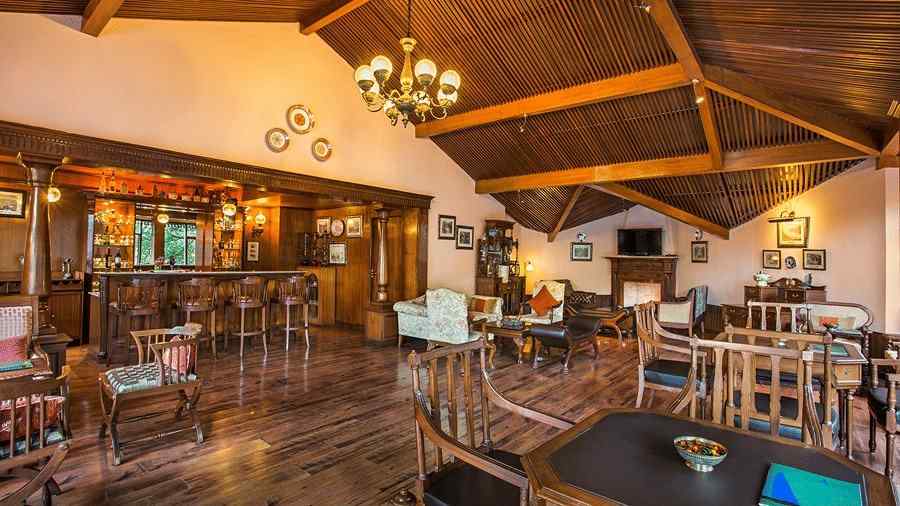 A bar and lounge area in naini retreat, nainital. The room features a wooden bar, comfortable seating arrangements, a fireplace, and a television. The overall ambiance is warm and inviting.