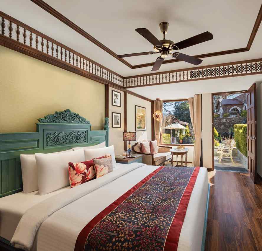 An image featuring premium Garden Room at naini retreat, nainital, A cozy and inviting hotel room with a king-size bed, The room features a small sitting area with a sofa and a side table, as well as a large window overlooking a garden.