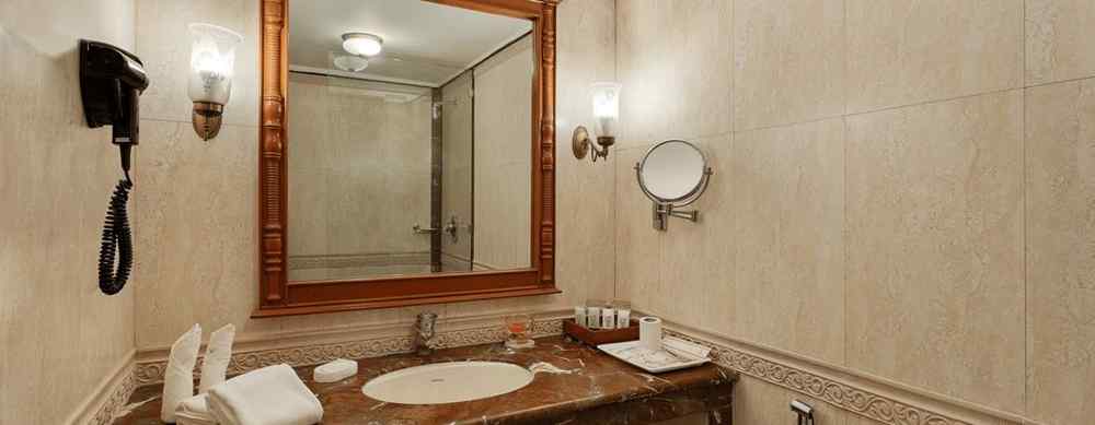 A spacious bathroom with a large mirror, a marble vanity, and a toilet. The walls are decorated with wallpaper and there is a wall-mounted phone. 