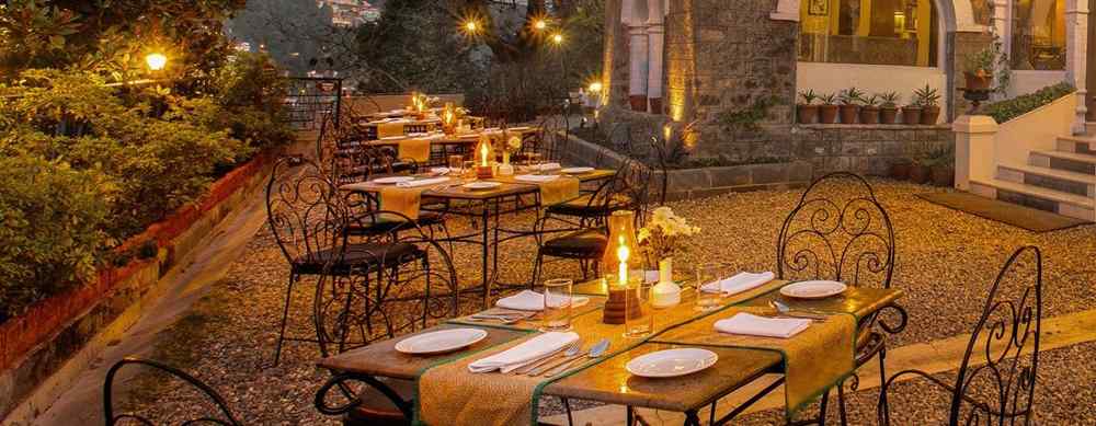 Pairs of tables places with chairs to accommodate up to 4 people on a set, in a outdoor setting in front of a house's entrance.