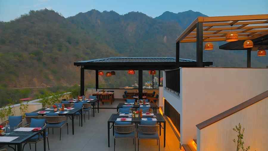 Open air dining space at The Terrace, Aloha on the Ganges, Rishikesh, with neatly arranged tables, rooftop seating, and scenic mountain views.