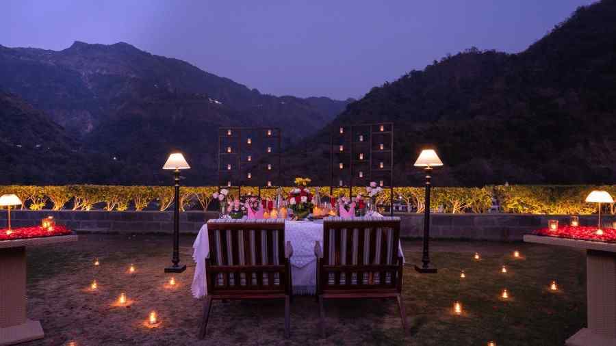 A dinner setup outdoors with a table adorned with candles and flowers,he backdrop is a beautiful mountain range at dusk.