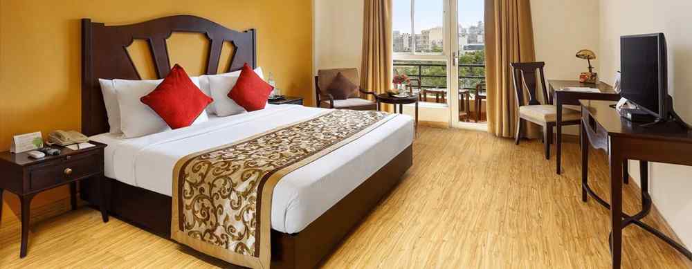 A side angle image of the room featuring a king size bed, coffee table and a large window enabling the outdoor view.