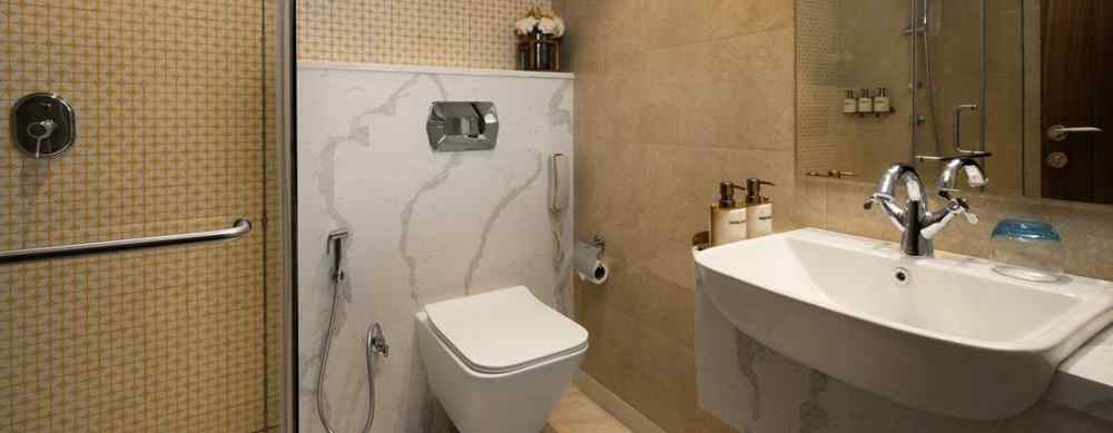 An image of a modern bathroom with a toilet, sink, and shower. The walls are tiled and there is a large mirror above the sink.