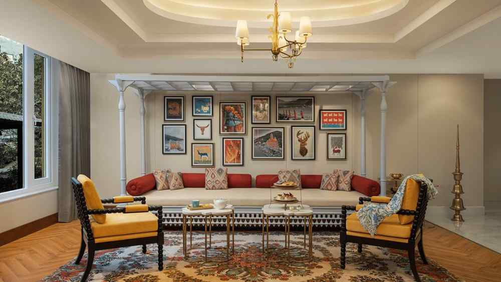 Elegant living room at Aloha on the Ganges Resort with sectional sofa, red and beige cushions, framed artwork wall, yellow armchairs, chandelier, and patterned rug.