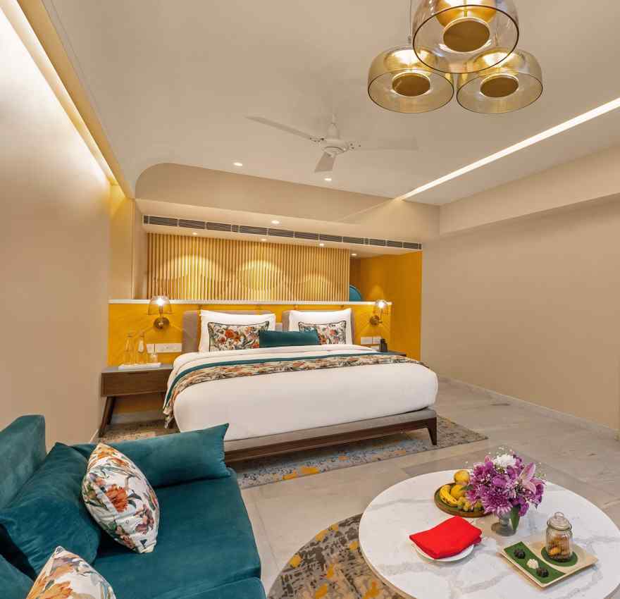 A n image of luxurious hotel suite with king bed, sofa, coffee table, and stylish decor.
