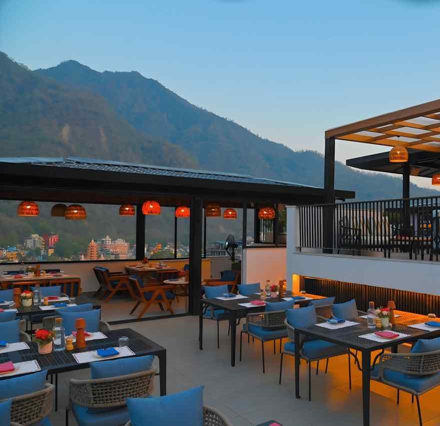 Rooftop dining area at The Terrace, Aloha on the Ganges, Rishikesh, featuring outdoor seating, illuminated staircase, and mountain views at dusk.