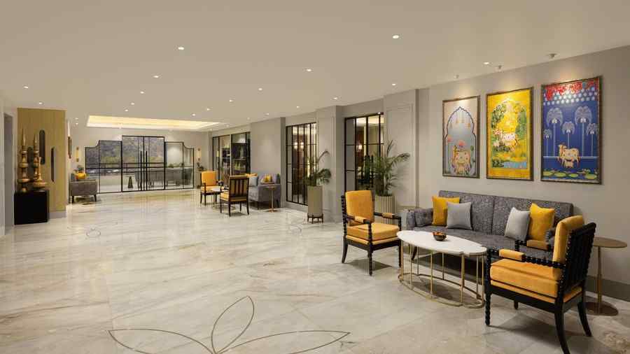 Spacious hotel atrium with marble floors, yellow-accent seating, framed artwork, and warm recessed ceiling lighting creating a modern lounge ambience.