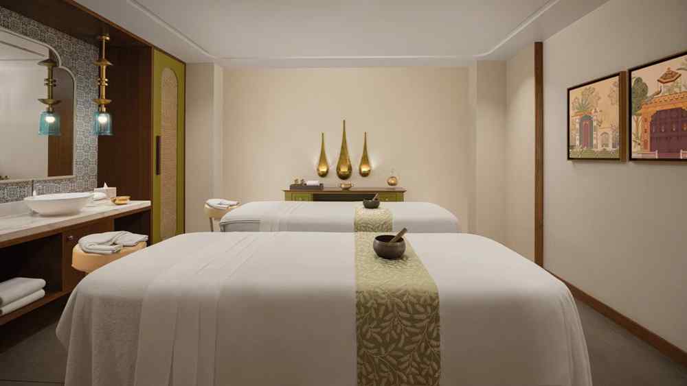 Relaxing spa room at Aloha on the Ganges Resort with two massage tables, patterned runners, warm lighting, decorative vases, pendant lights, and minimalist decor.
